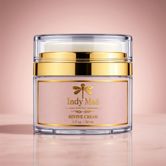 Indy Maé Revive Cream in a clear jar with a gold metallic lid and a pale pink label, set against a solid pale pink background.